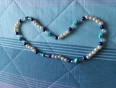 Ogrlica z belimi perlami, vmes so temno modre perle in kamen tirkizne barve