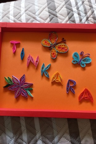Tinkara - V tehniki quilling narejeno ime Tinkara, zraven sta 2 metuljčka in rožica. Vse je v okviru iz šeleshamerja